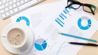 デスクの上のコーヒー紙の書類、パソコン、メガネ