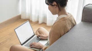 ソファの前でパソコン作業を行う女性